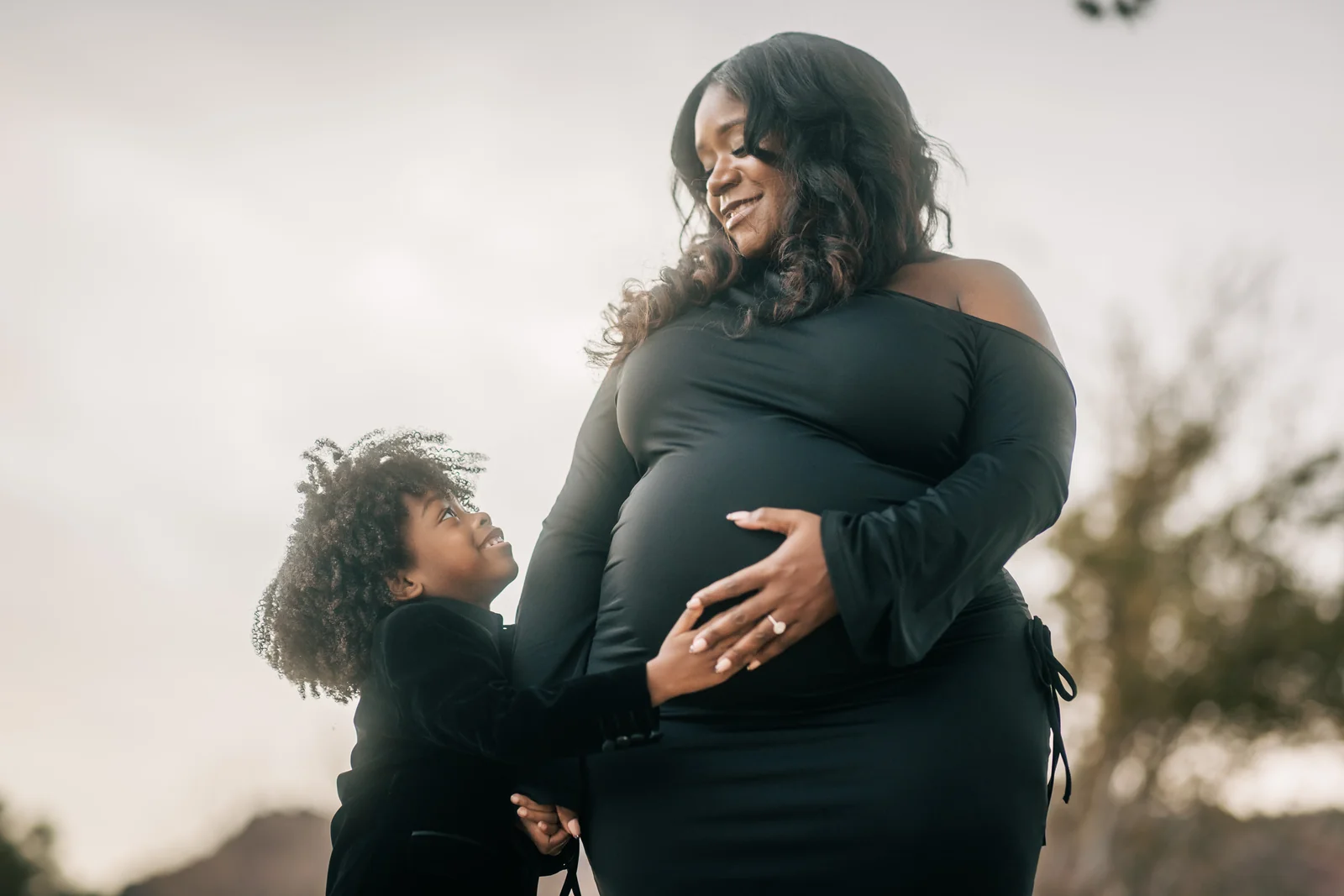 Child looking up at Mom with a hand on her bump during a maternity session in Henderson.