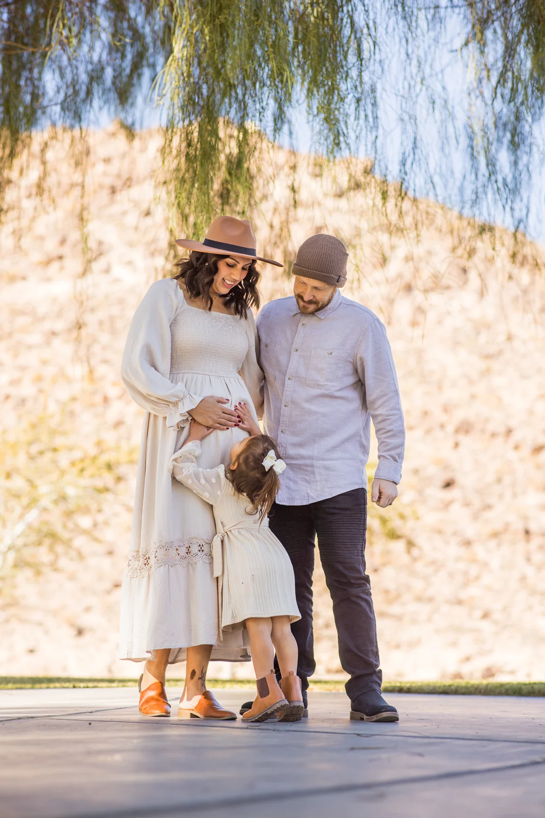 Parents standing together as their child reaches toward Mom’s bump during a maternity session in Henderson.