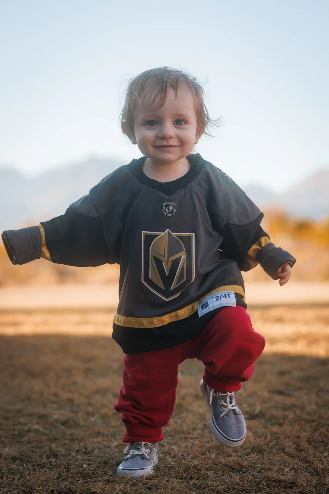 Toddler in a Golden Knights jersey walking toward the camera in a Summerlin park