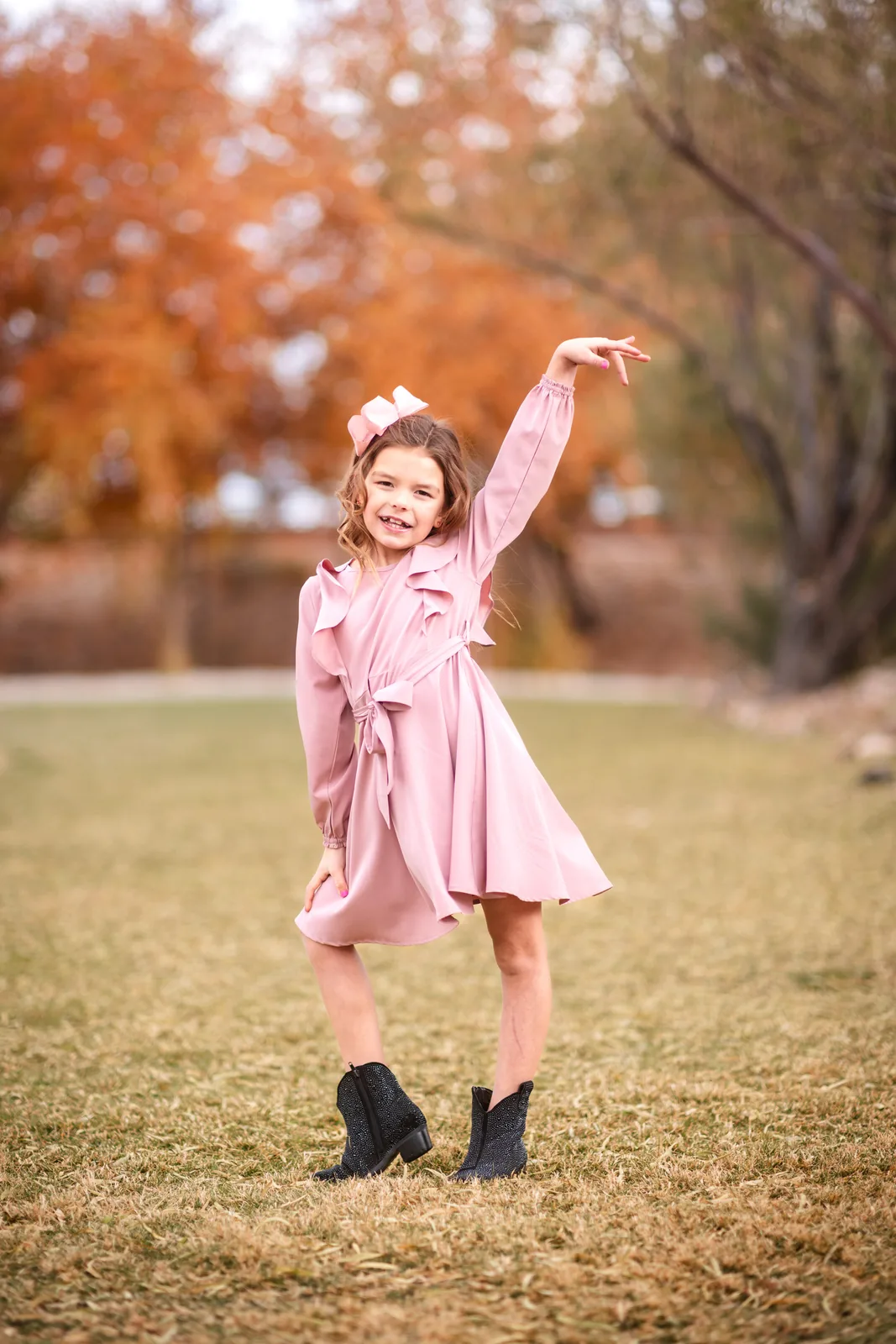Girl in a pink dress striking a playful pose under fall trees in Summerlin
