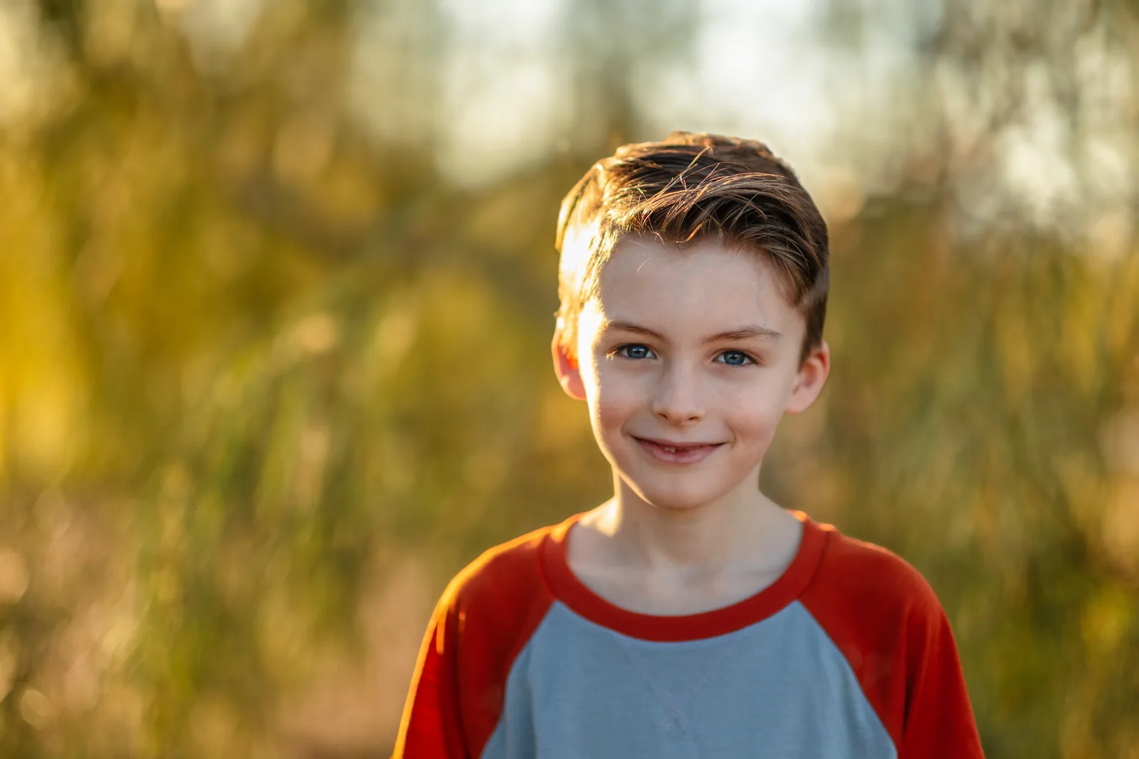 Smiling boy in a red and gray shirt against a soft, blurred fall background at Tule Springs