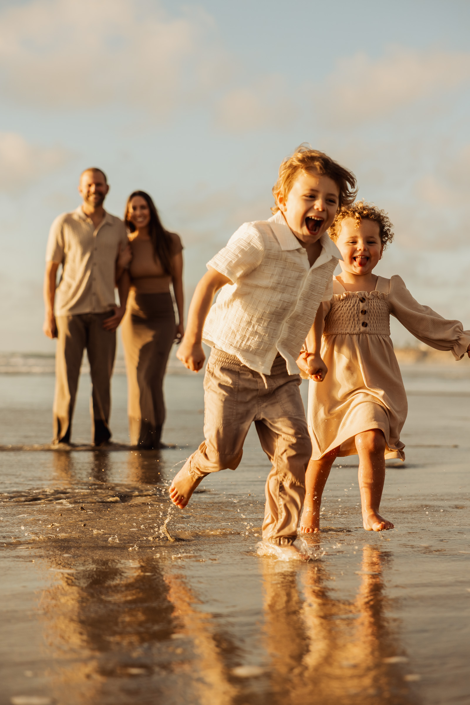 Two kids splashing along the Carlsbad shoreline while their parents watch
