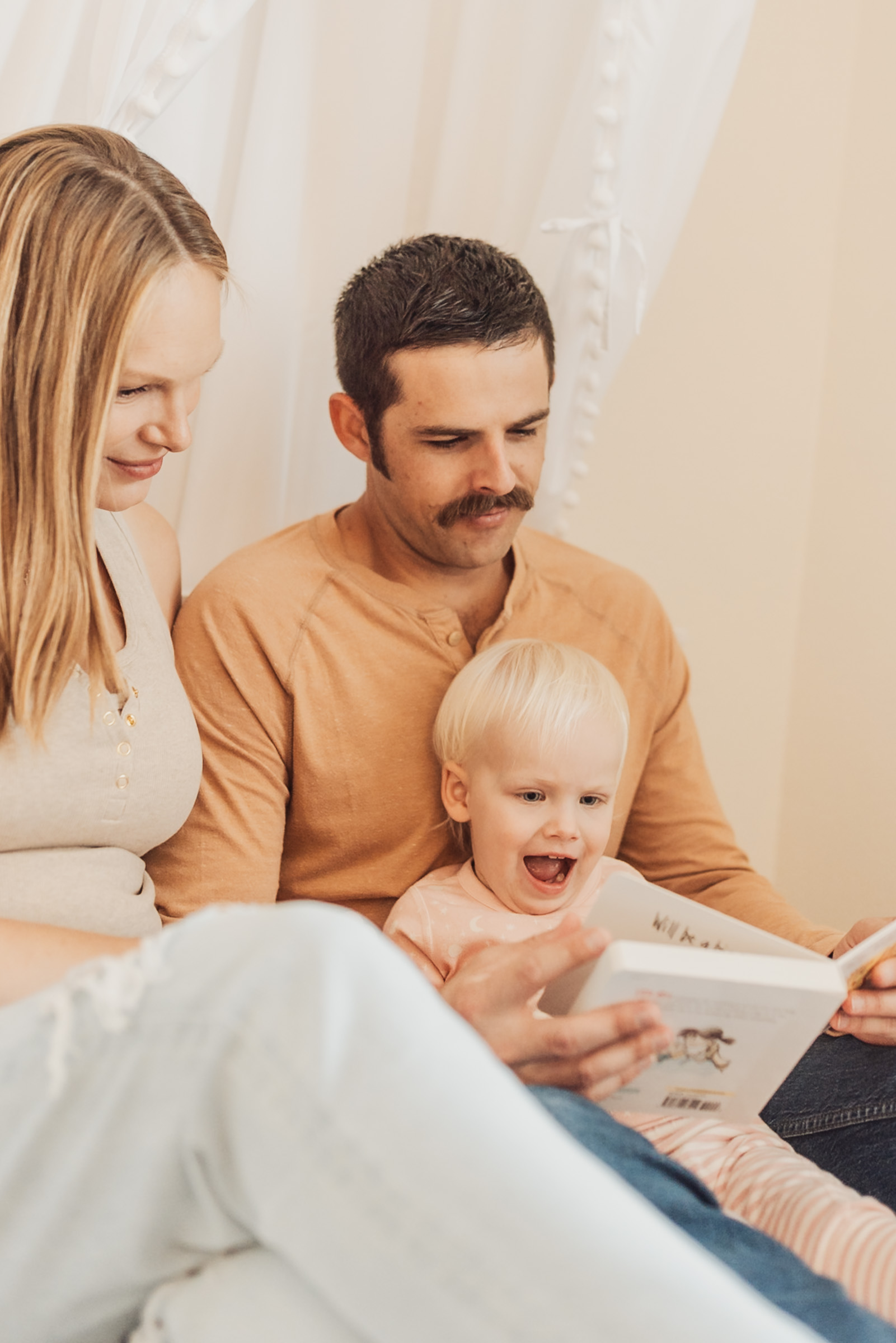 Parents reading a picture book with their laughing toddler