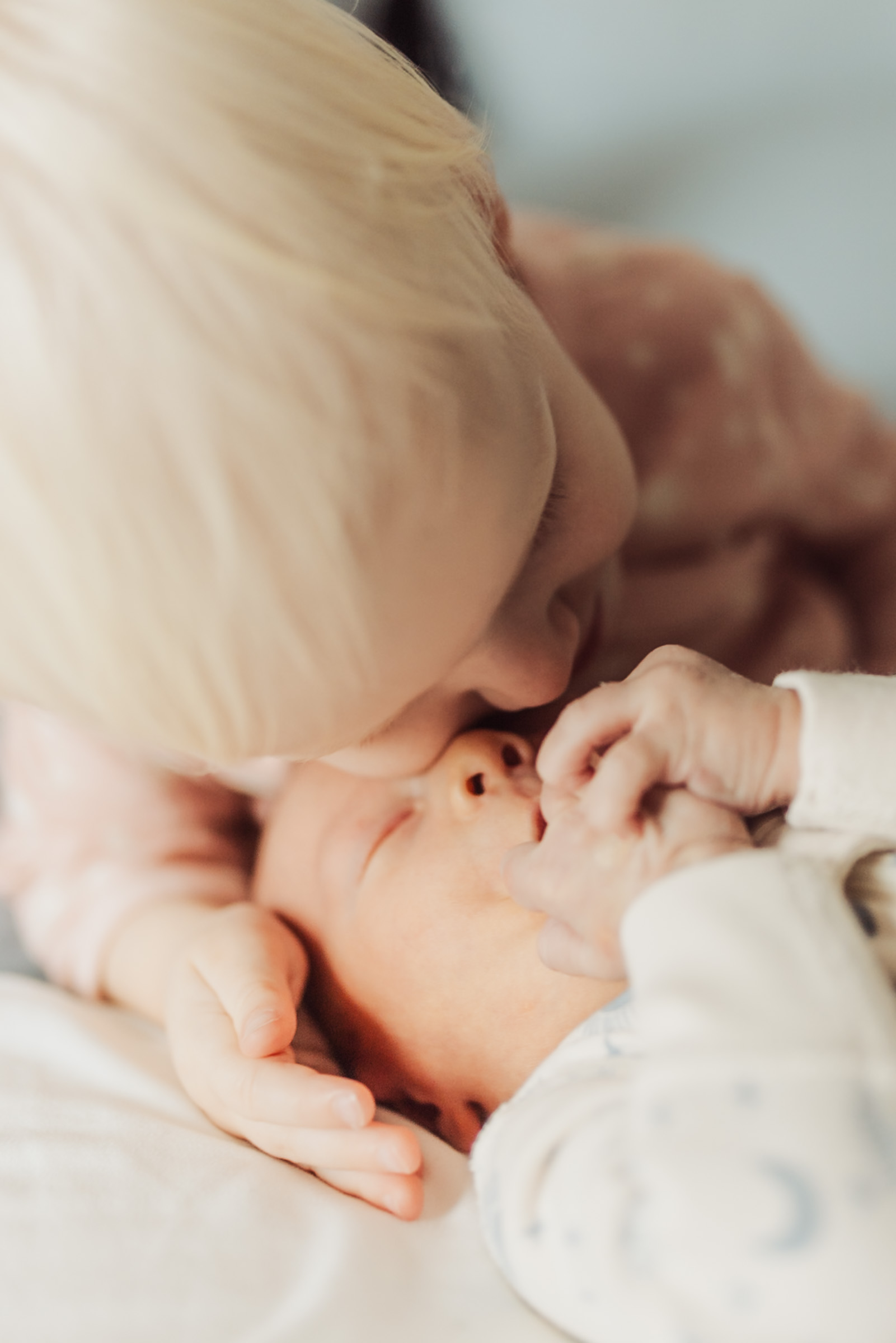 Blond toddler leaning in to kiss a newborn on the cheek
