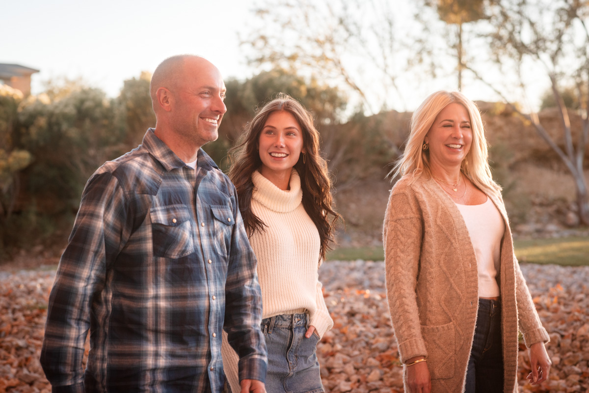 A family of three standing together among autumn trees.
