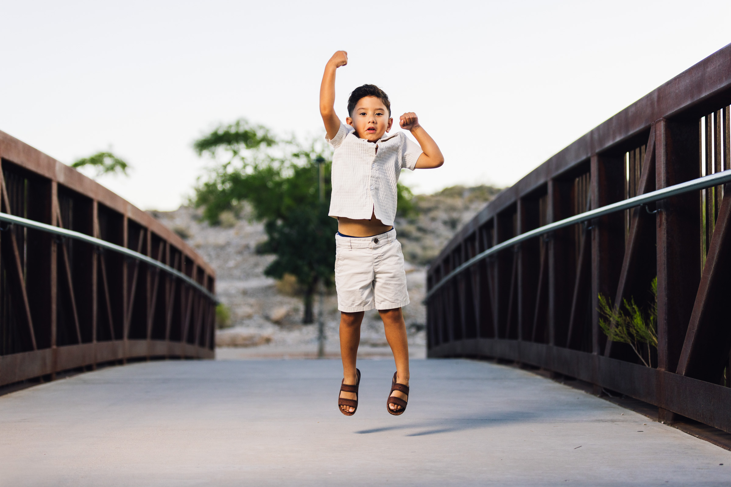 Young boy jumping mid-air on a wooden footbridge with his arm raised during a Las Vegas photo session