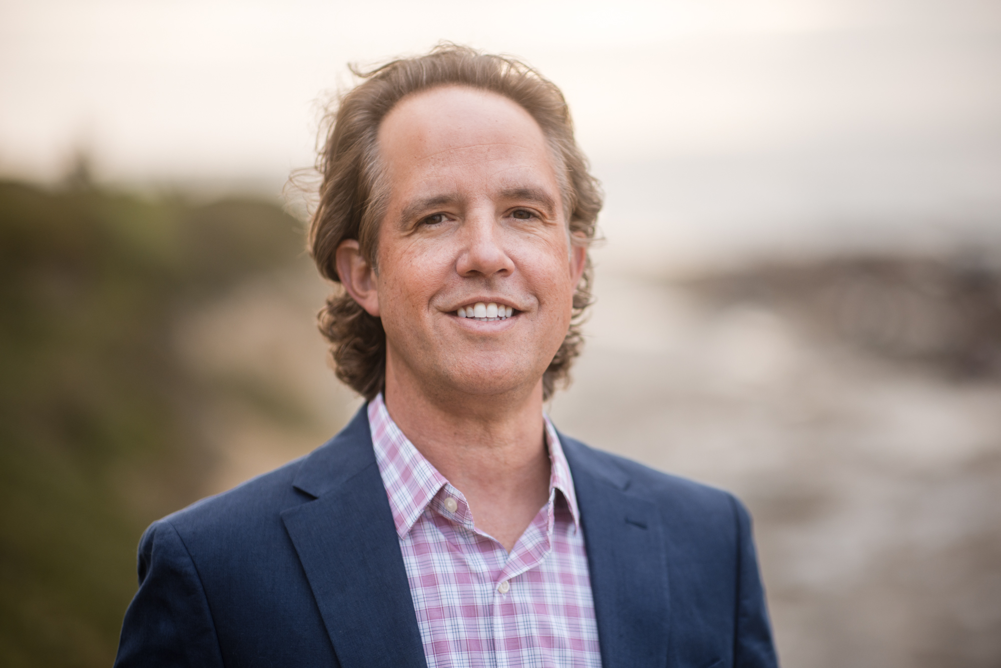 Outdoor headshot of a smiling man wearing a navy blazer.