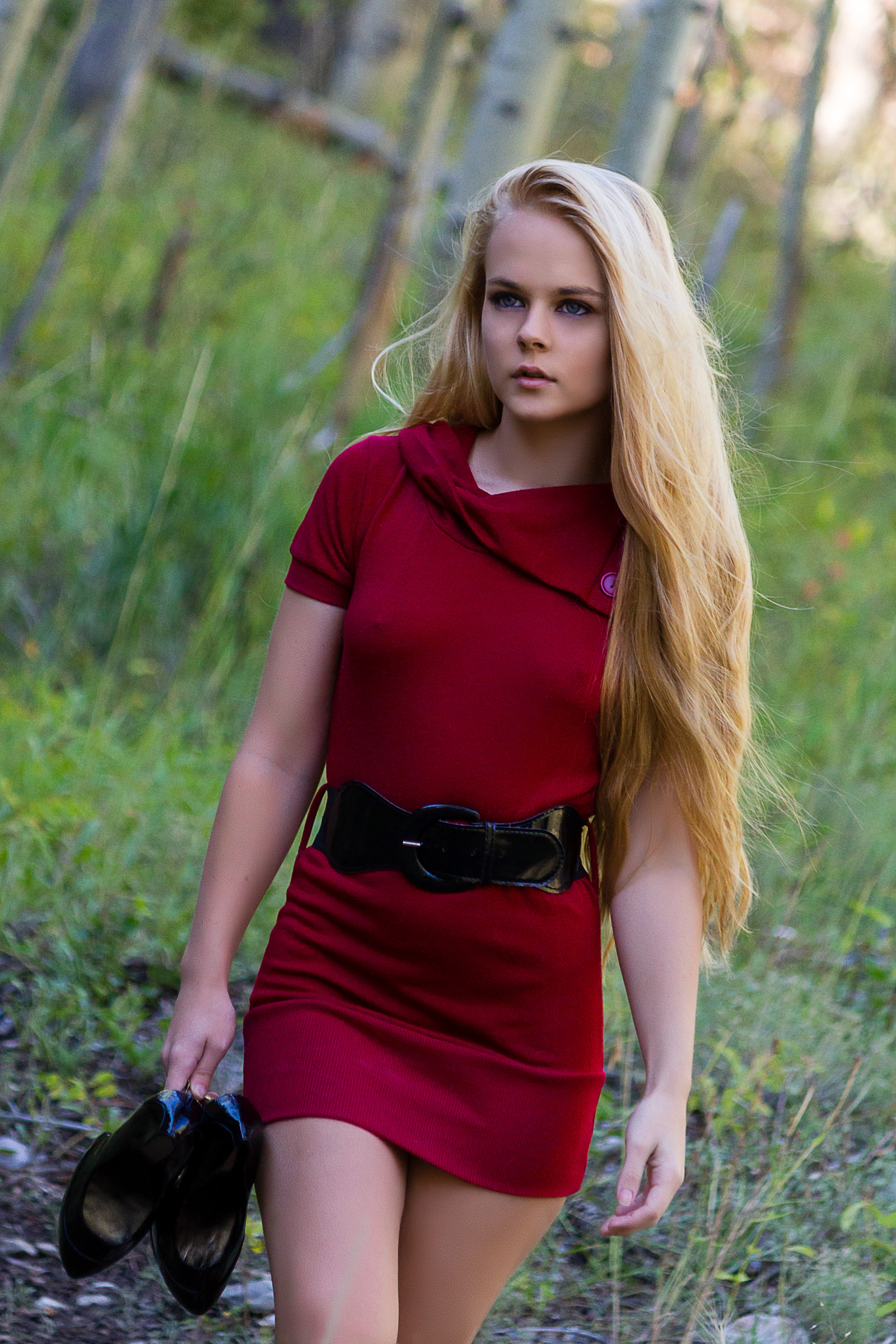 Young woman in a red dress holding her heels as she walks through a green forest meadow on Mount Charleston