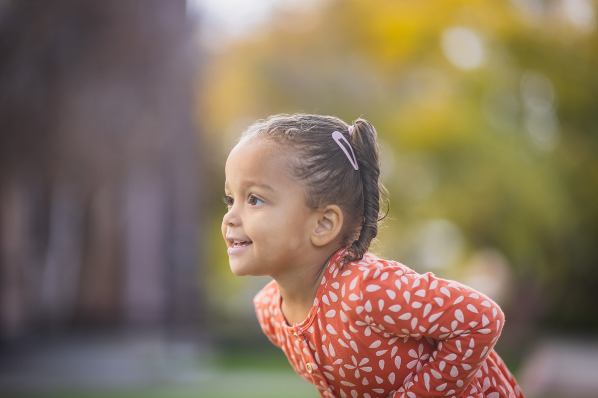 Profile portrait of a young girl wearing a red patterned shirt outdoors.