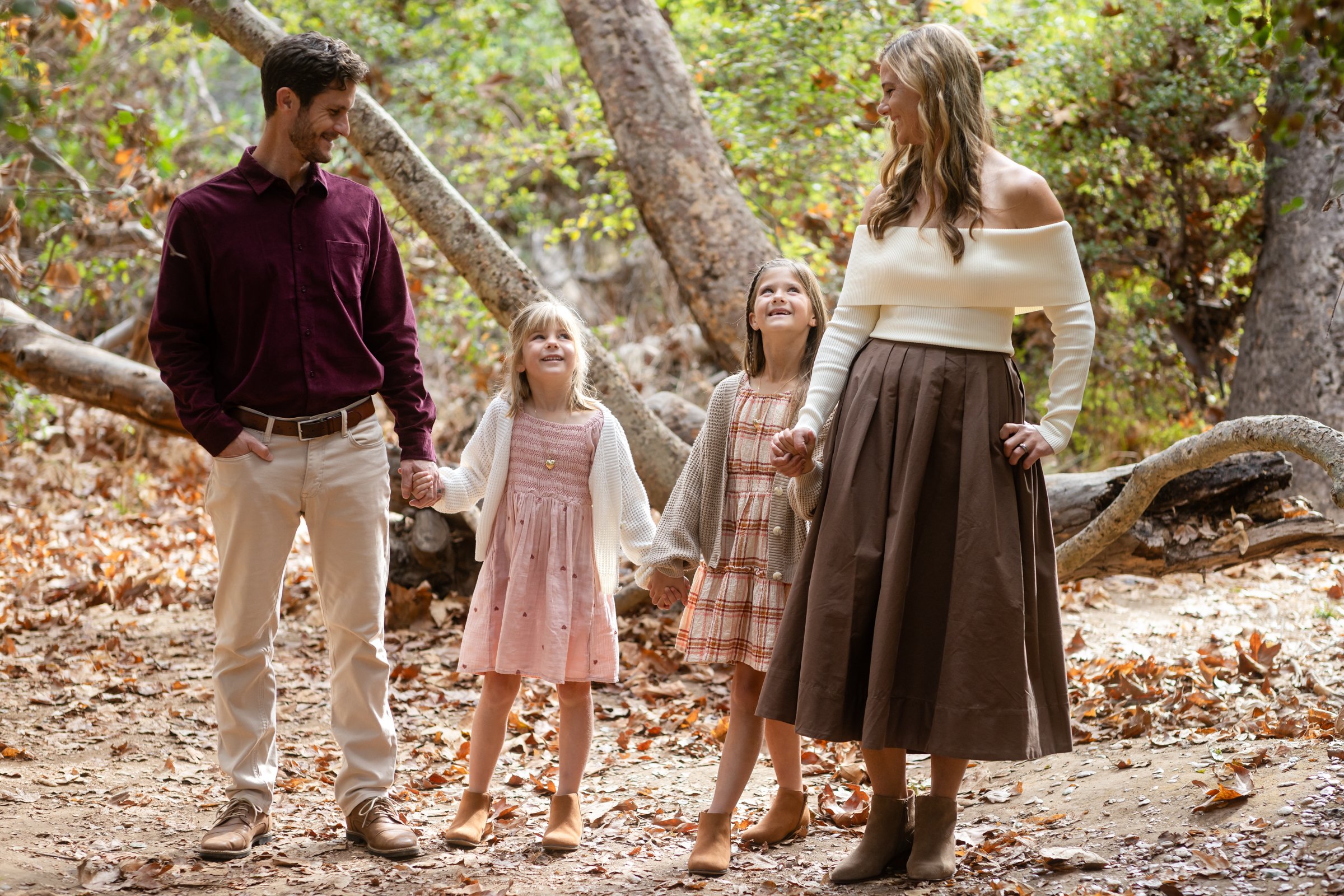 Two parents holding hands with their daughters on a wooded path.