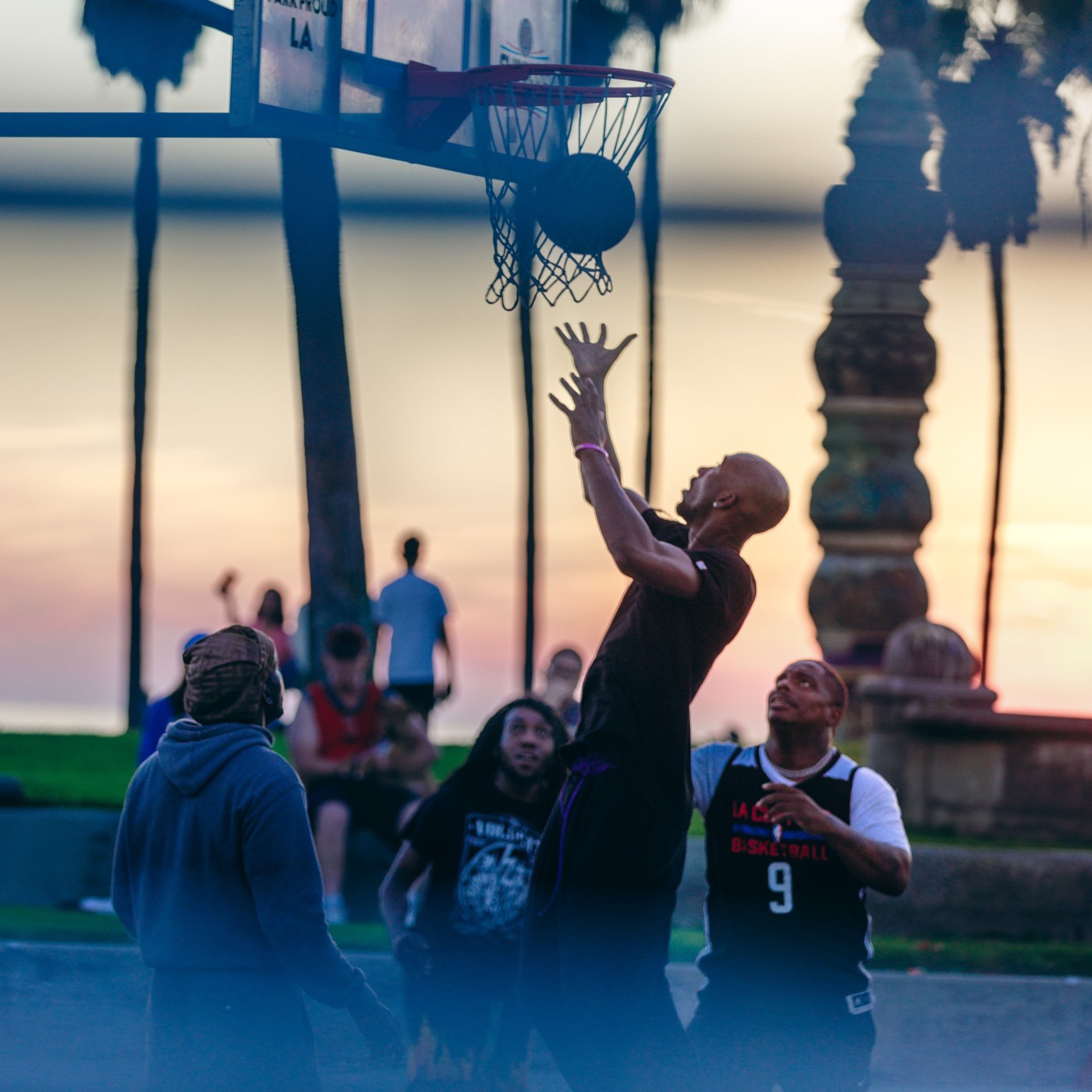 A basketball player reaching toward the hoop at sunset.
