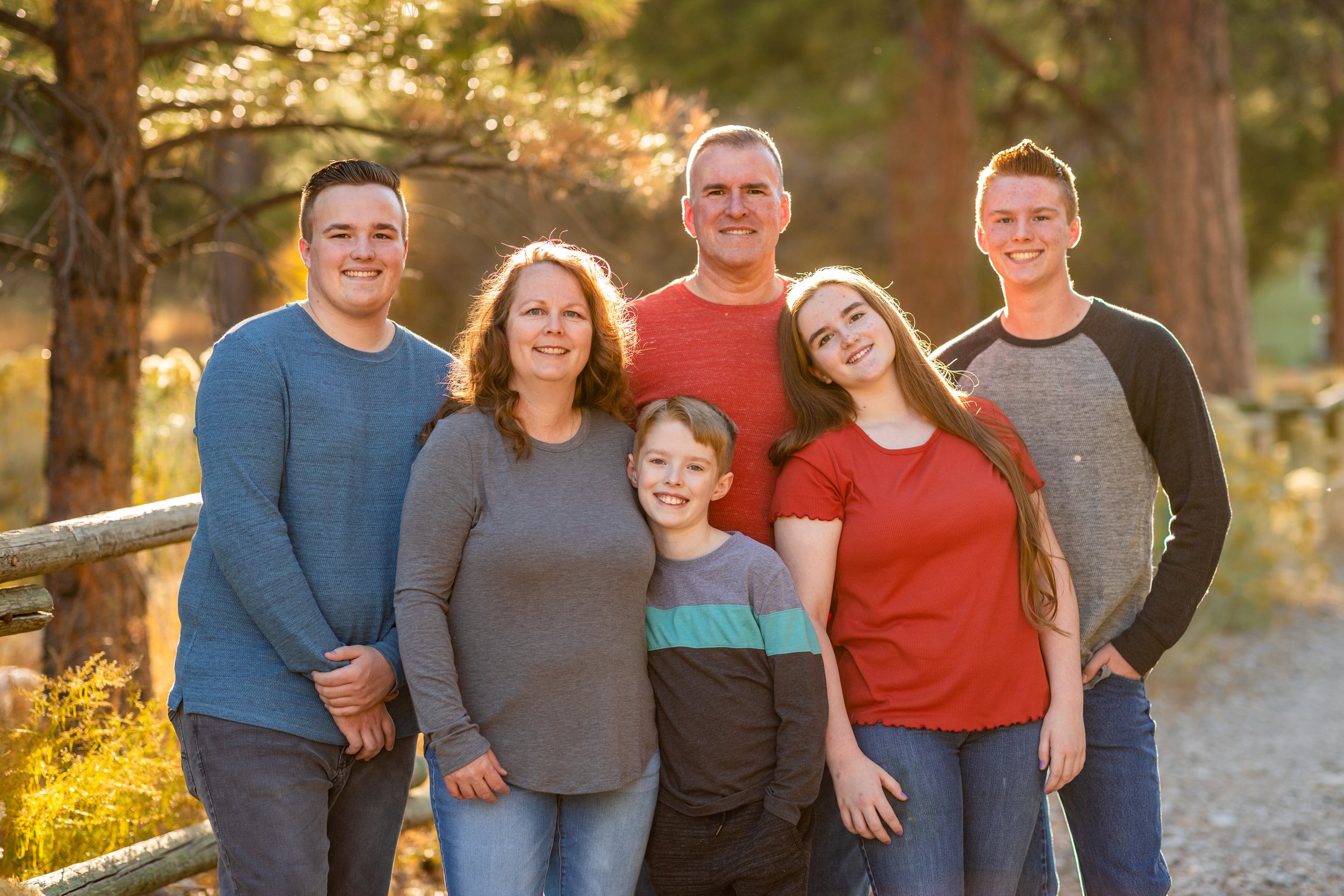 A family of six gathered beside a wooden fence among autumn trees.