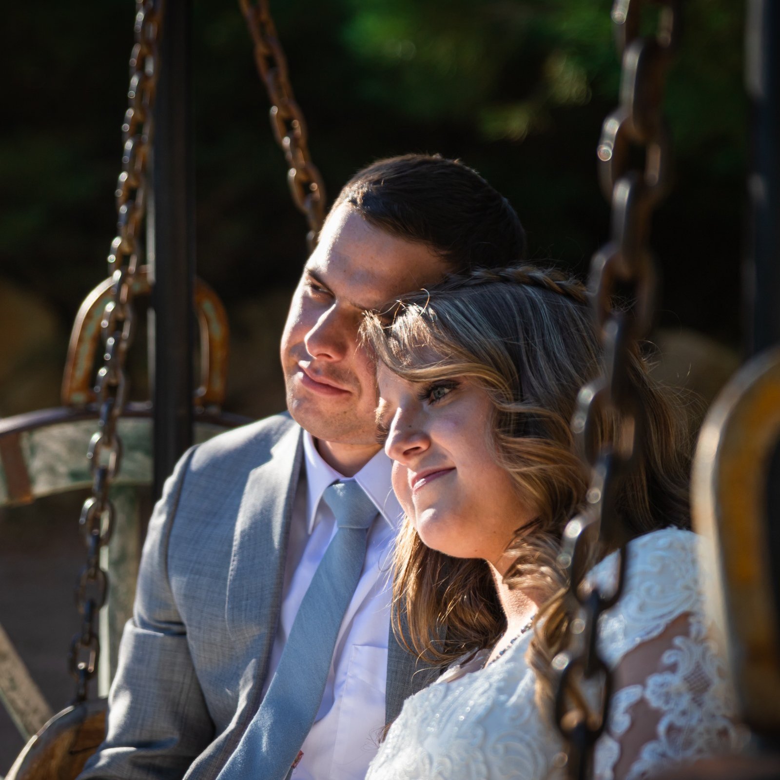 A wedding couple sitting together on a garden swing.