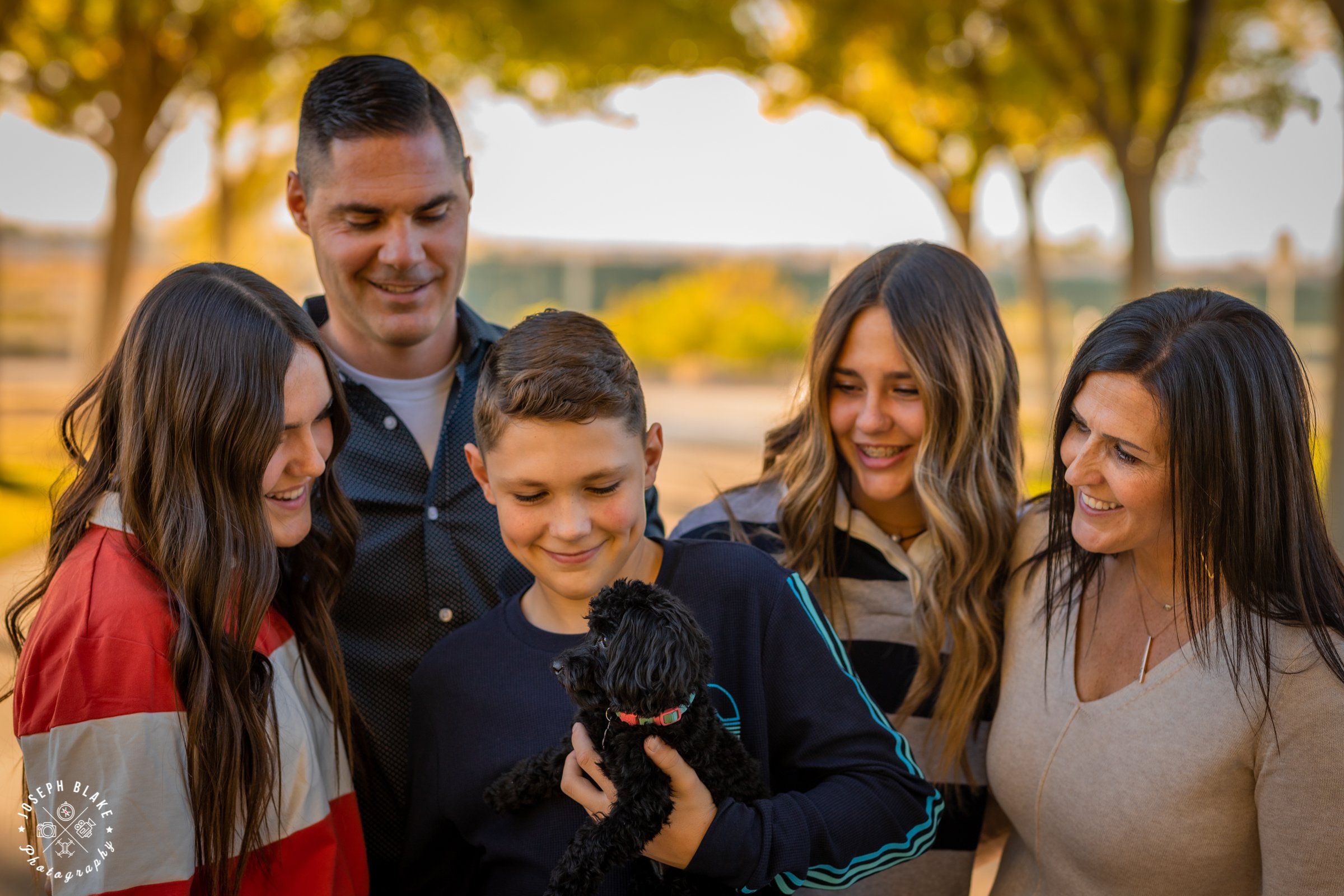 A family of five looking at a small dog held by their son.
