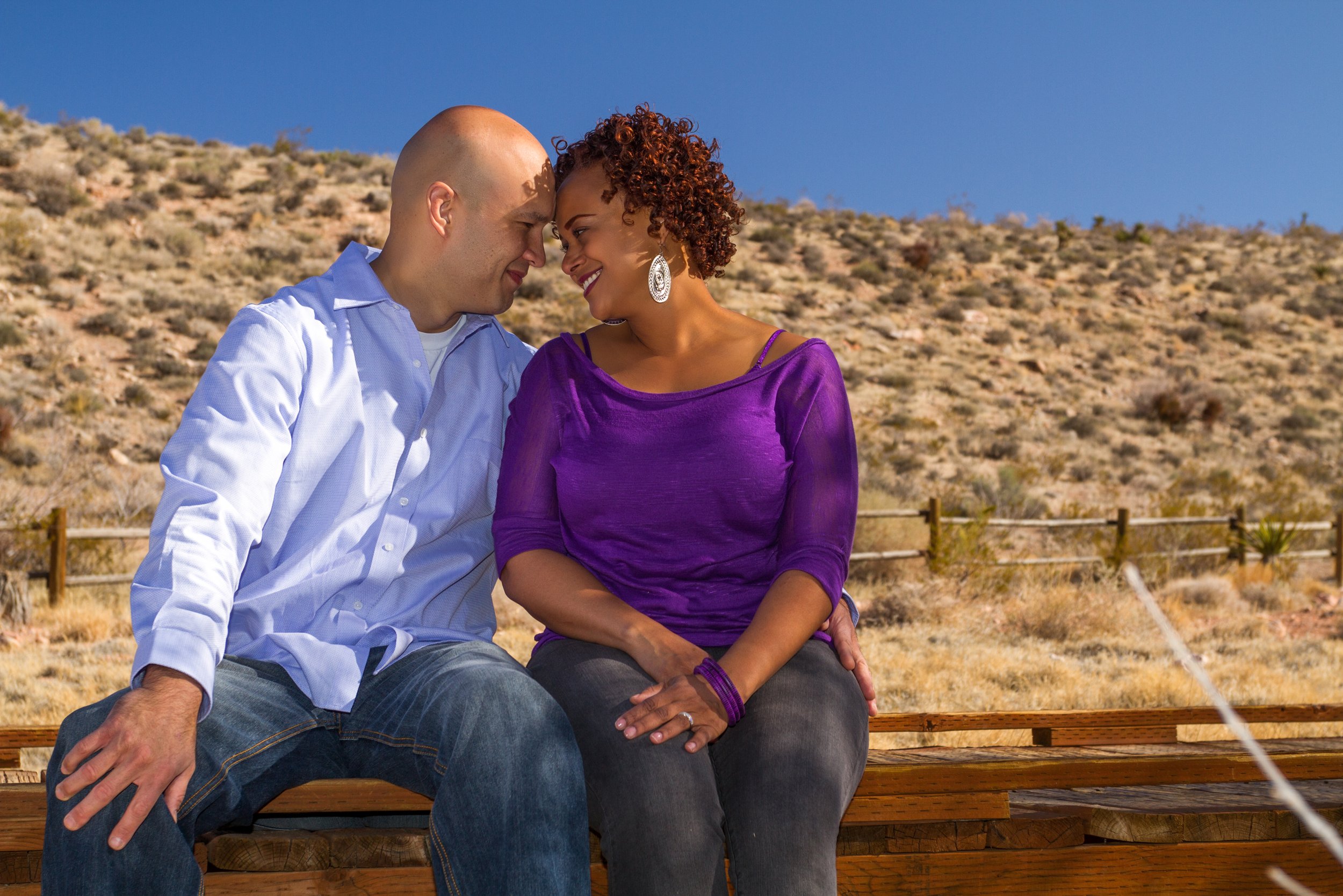 A couple sitting close together on a bench in a desert landscape.