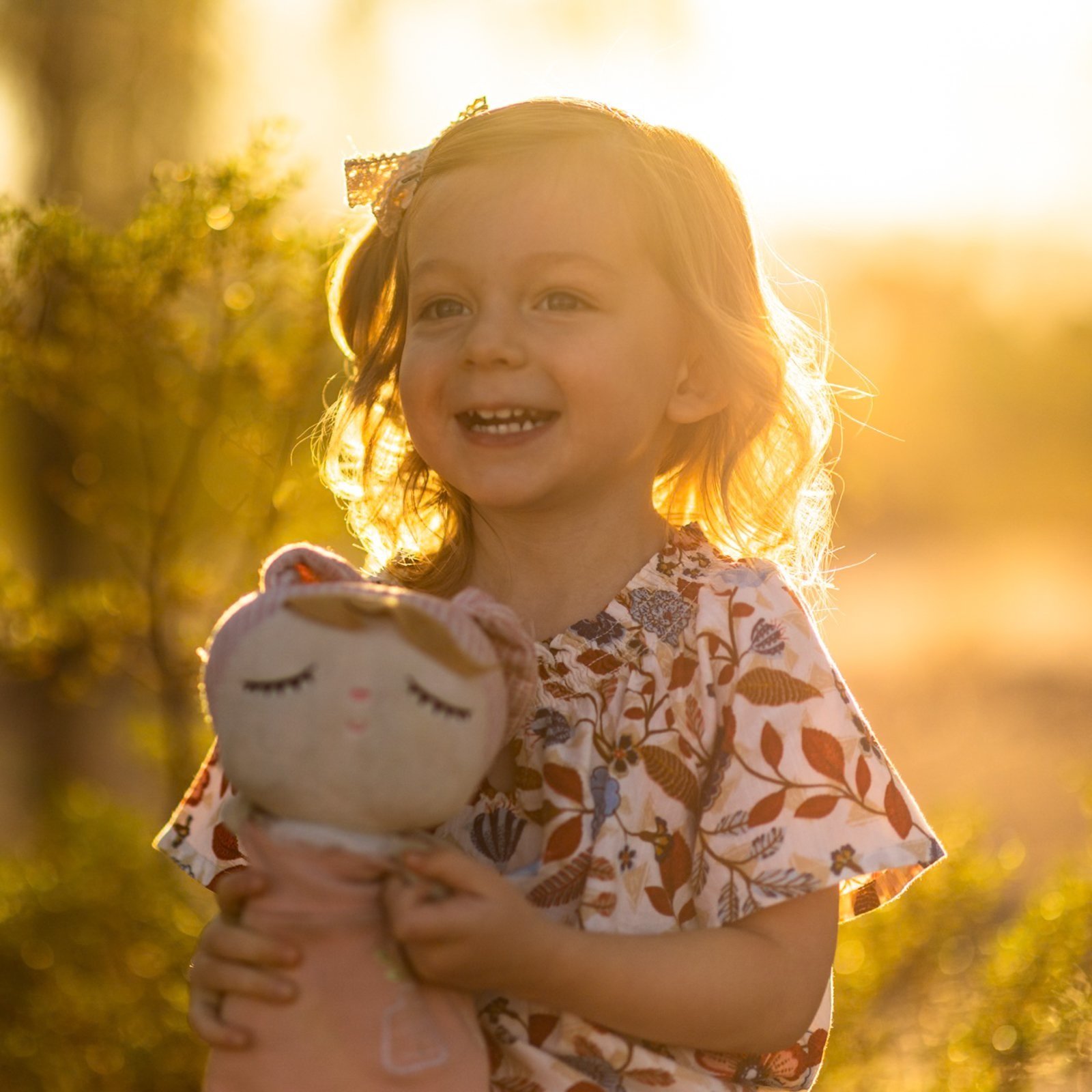A young girl holding a stuffed toy in warm, backlit evening light.