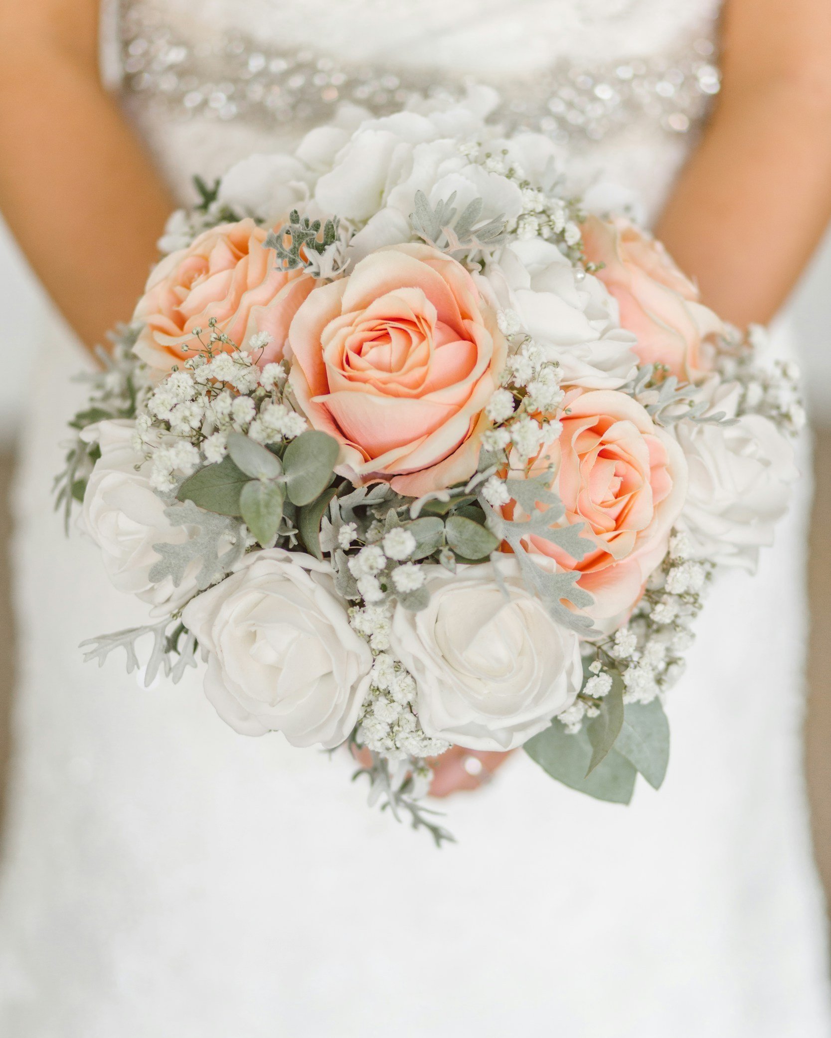 A bride holding a bouquet of peach and white roses.