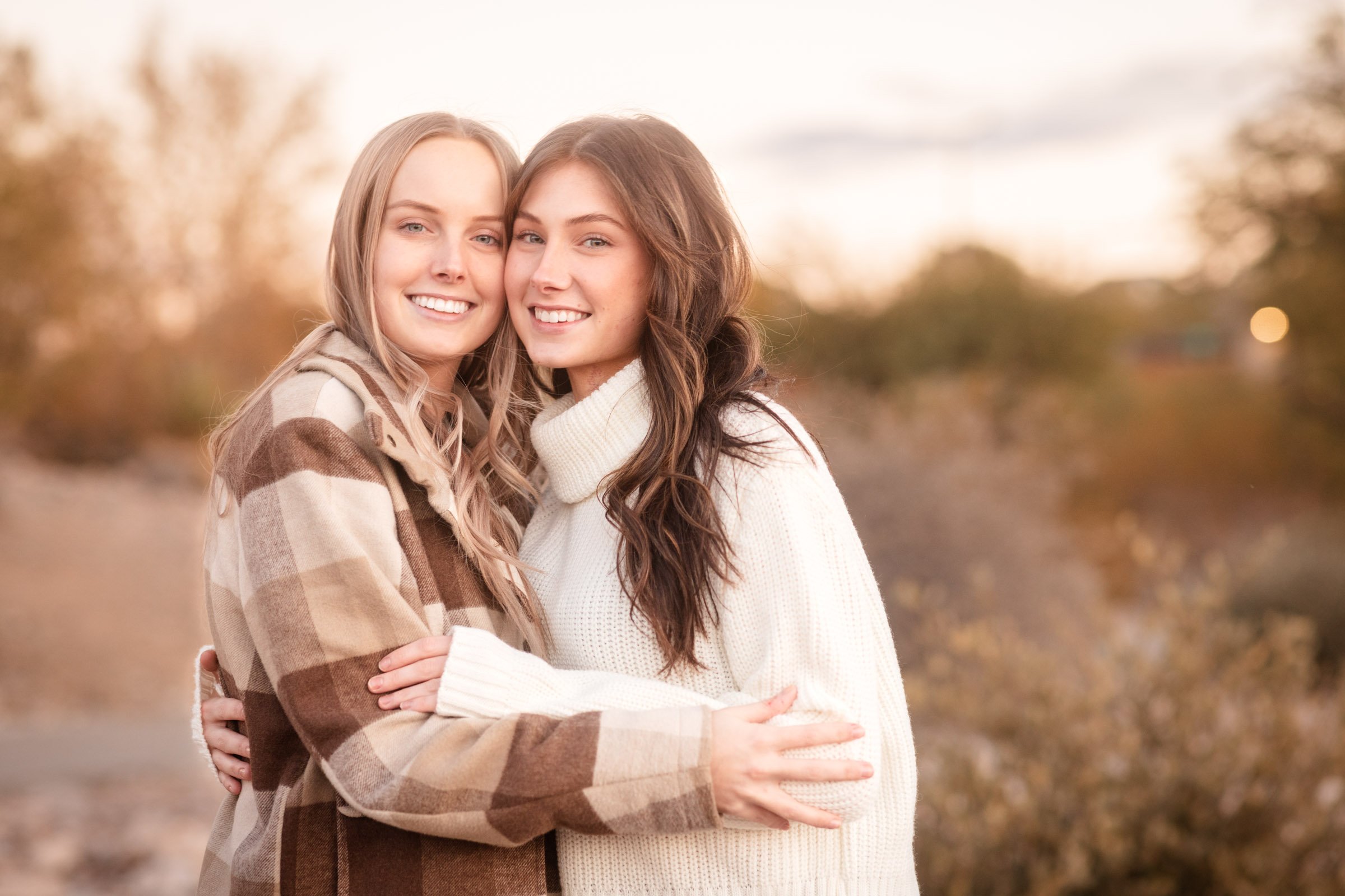 Two women embracing and smiling in warm evening light.